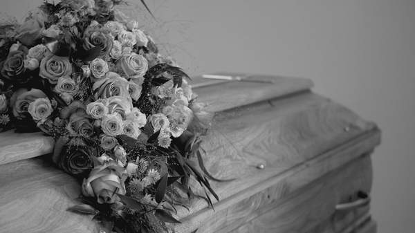 A close-up of a floral casket spray arrangement made of roses resting on a polished wooden casket