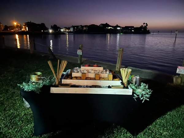 A custom s'mores food bar table set up outdoors at night along a waterfront lawn with a tiered display