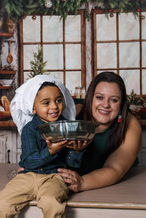 A professional portrait of a smiling woman and a young boy wearing a white chef's hat, holding a Bundt cake pan
